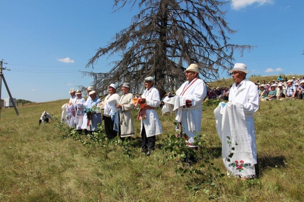 Фото закамских удмуртов, празднующих сабантуй, наряженных в белые одежды в поле у старой ели