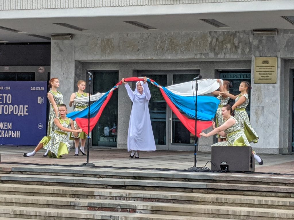 Фото выступление девушка в белом одеянии проходит под флагом россии