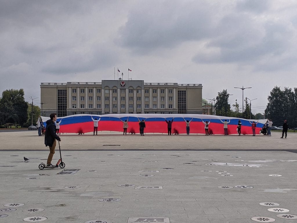 Фото огромного флага россии перед зданием правительства, на переднем плане проезжает мужчина на самокате