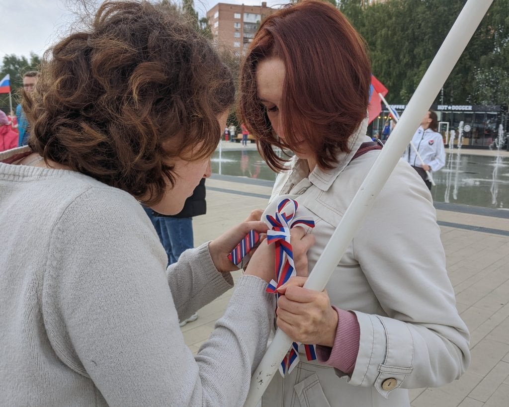 Фото девушка-волонтёр прикрепляет флаг россии на грудь женщине