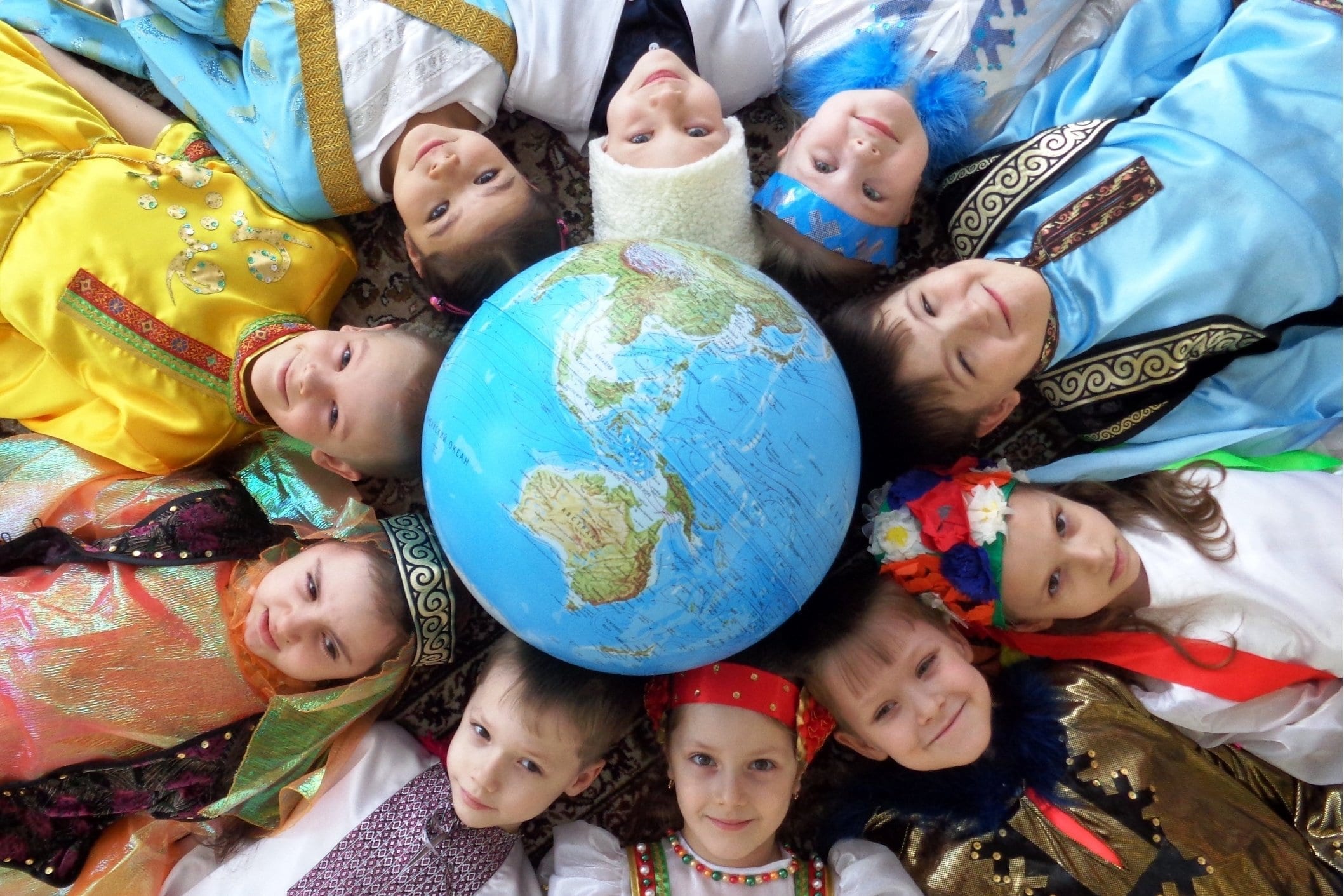 Фото дети в разных национальных костюмах лежат вокруг глобуса