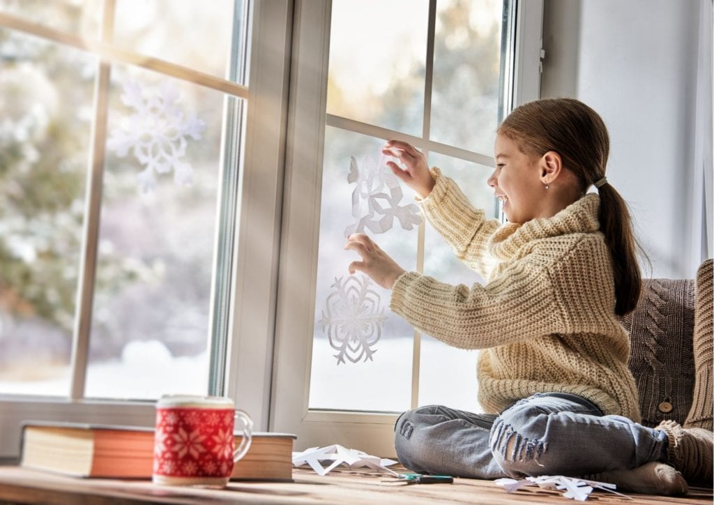 Фото девочка вешает вырезанную из бумаги снежинку на окно
