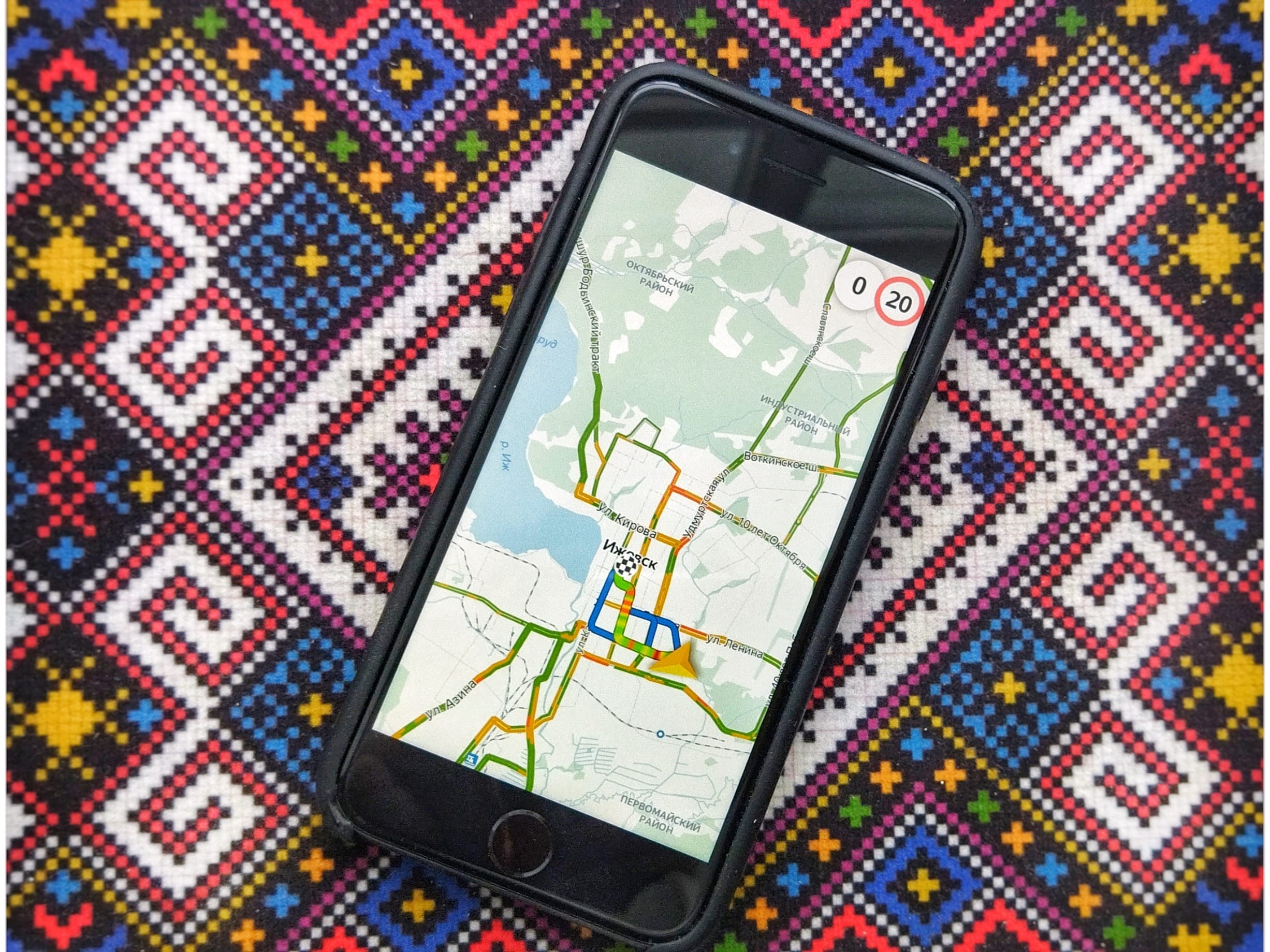 Фото смартфона с запущенным приложением яндекс навигатор на фоне разноцветного коврика